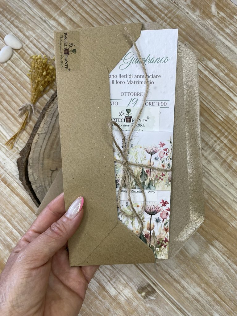 Partecipazione di matrimonio in carta piantabile inserita in una busta kraft rustica. La partecipazione presenta un elegante design floreale, con illustrazioni delicate di fiori selvatici, e include un cordino di spago naturale che richiama lo stile eco-friendly. La busta in carta riciclata, insieme alla grafica raffinata e ai materiali sostenibili, riflette il tema di un matrimonio green e rispettoso dell'ambiente.
