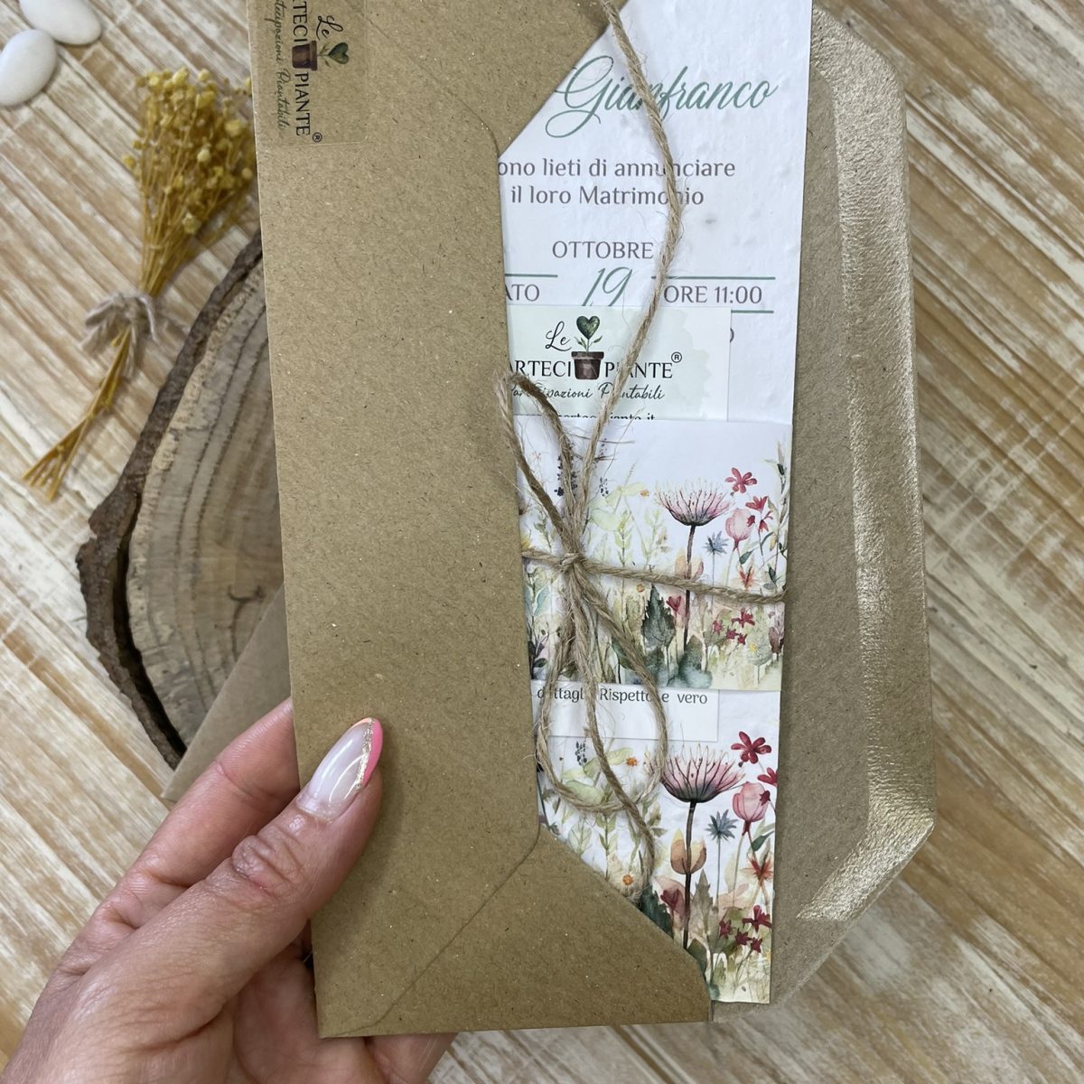 Partecipazione di matrimonio in carta piantabile inserita in una busta kraft rustica. La partecipazione presenta un elegante design floreale, con illustrazioni delicate di fiori selvatici, e include un cordino di spago naturale che richiama lo stile eco-friendly. La busta in carta riciclata, insieme alla grafica raffinata e ai materiali sostenibili, riflette il tema di un matrimonio green e rispettoso dell'ambiente.