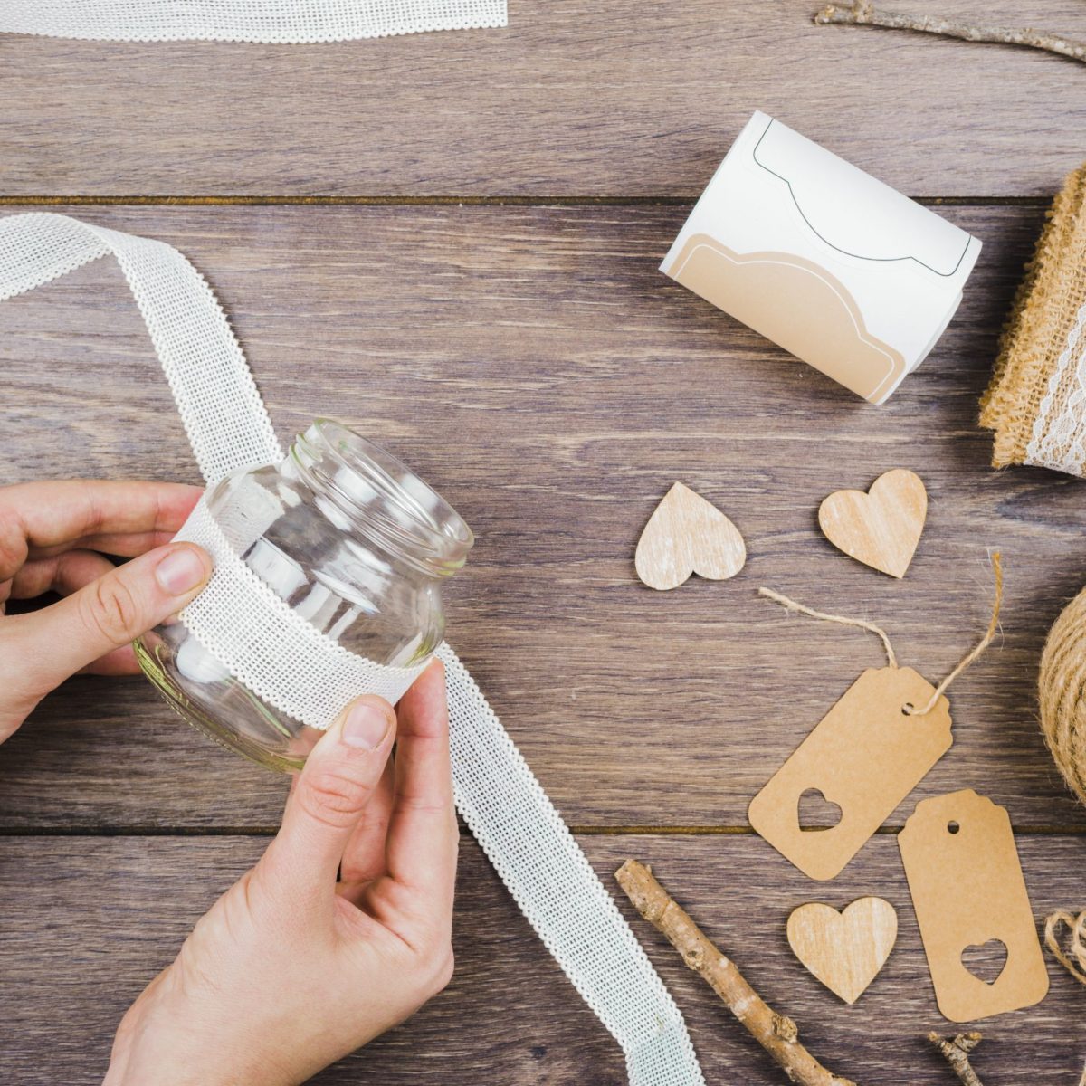 sposa fai da te - primo-piano-della-mano-della-donna-che-attacca-il-nastro-di-pizzo-bianco-sulla-bottiglia-di-vetro-sopra-la-scrivania-legno